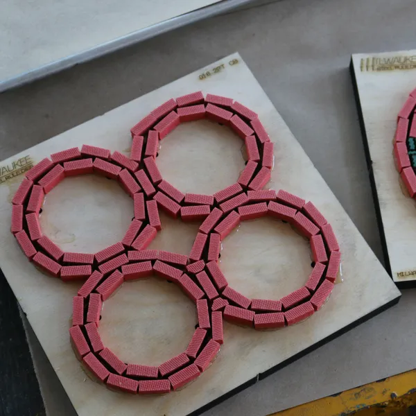 Two fresh steel rule dies on plywood die boards, one cutting four overlapping circles and one a single large circle, with the sharpened rule hidden inside red ejection rubber