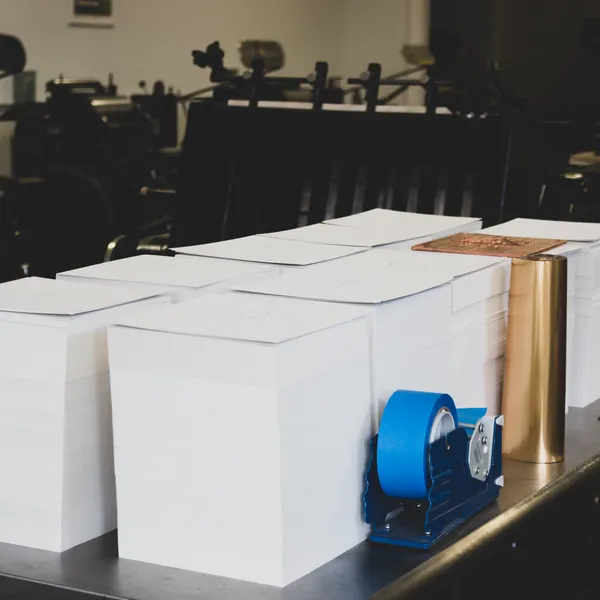 Stacks of cotton paper blanks staged for printing with a roll of copper foil alongside