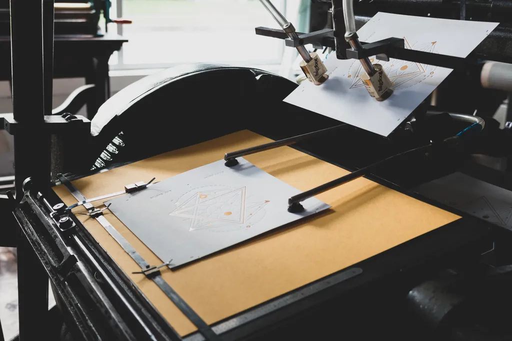 Platen press holding a freshly printed two-color geometric piece in the guides