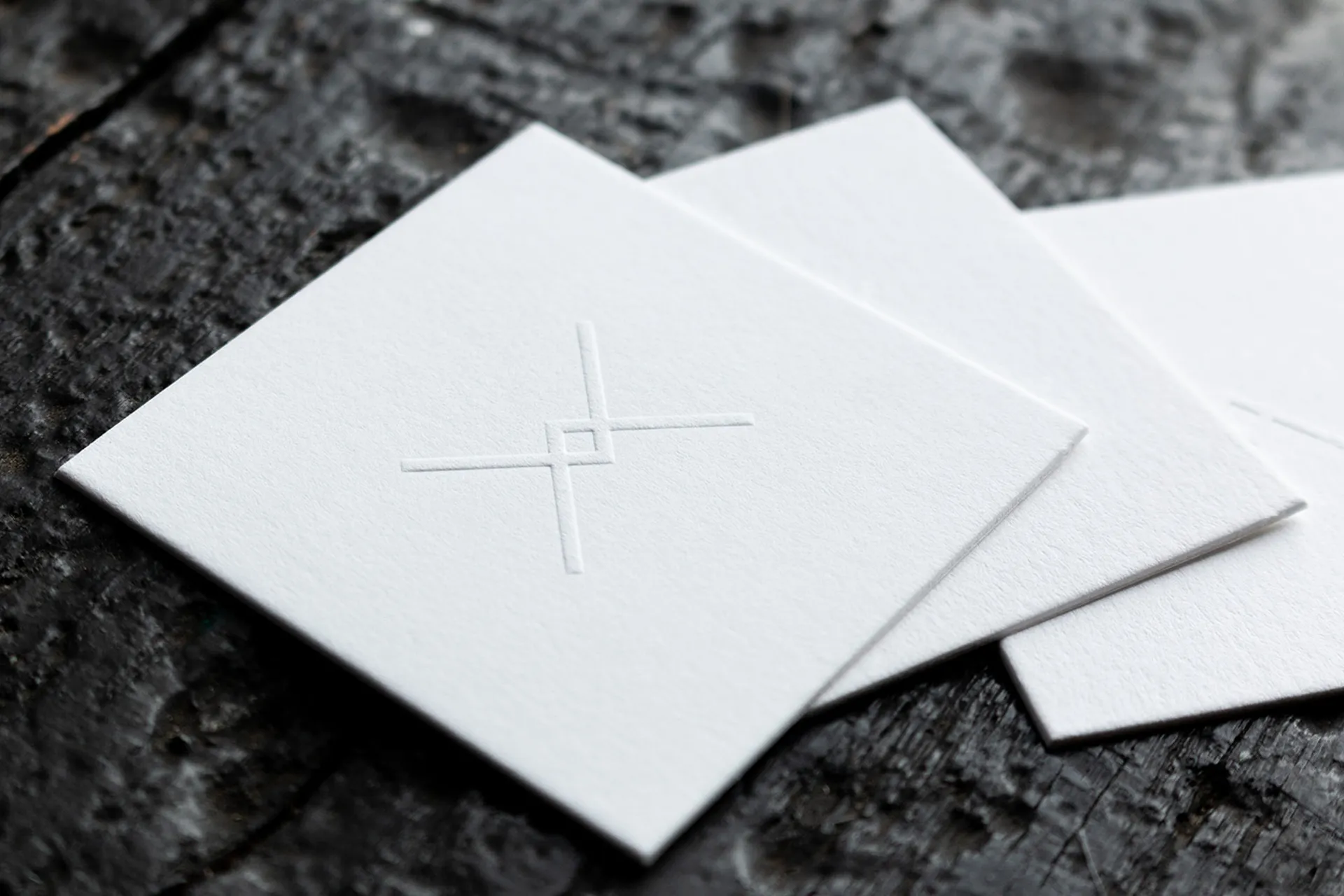 White business cards with blind embossed crosshair logo on thick cotton paper, fanned out on a dark textured surface