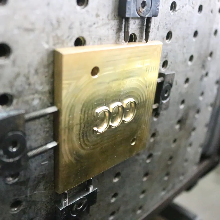 Brass embossing die engraved with three letter Cs, locked onto the honeycomb base of a press