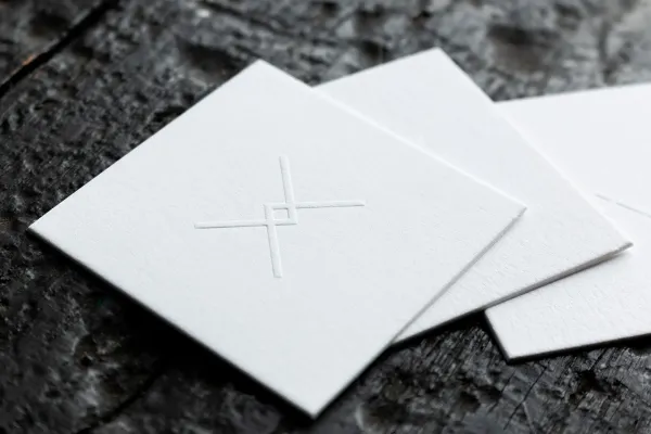 White business cards with blind embossed crosshair logo on thick cotton paper, fanned out on a dark surface