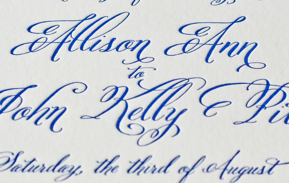 Macro detail of the flourished copperplate names showing the deep letterpress impression in cobalt blue ink on cotton paper