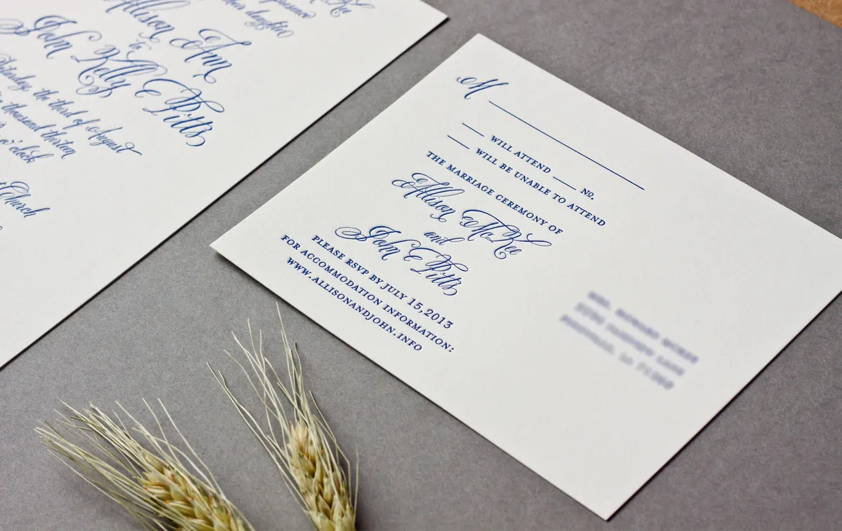 Letterpress RSVP card printed in cobalt blue on cream cotton stock, photographed at an angle with wheat sprigs