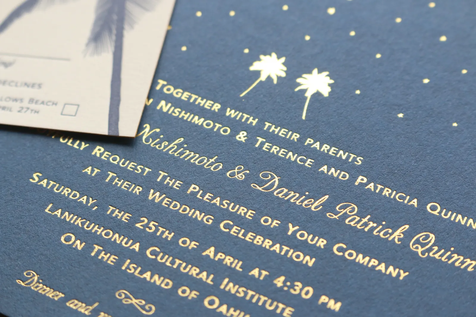 Angled view of the gold foil stamped typography and palm tree motif on the blue wedding invitation