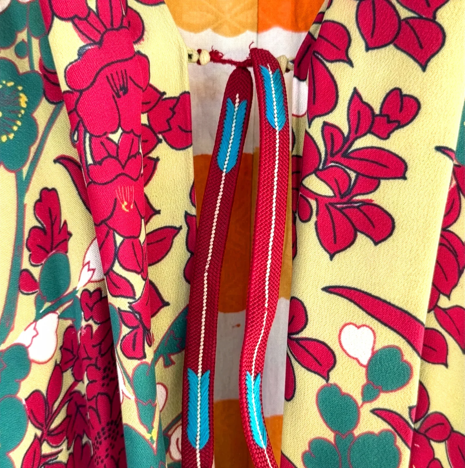 Closeup of vintage Japanese kimono fabric with red camellias and foliage on yellow ground, interior orange lining, and a turquoise and red woven tie