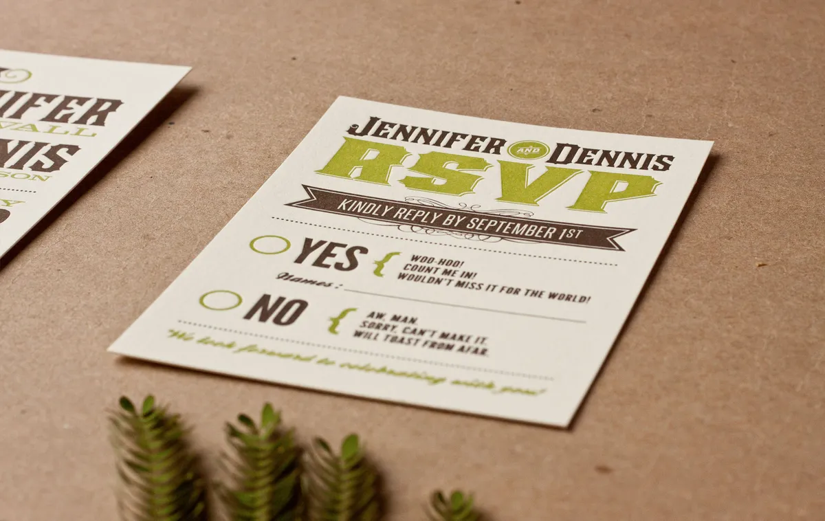 Angled view of the matching RSVP card in olive and espresso brown letterpress on cream cover stock with kraft and mimosa fern background