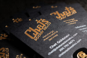 A black business card with white, gold and black foil stamping.