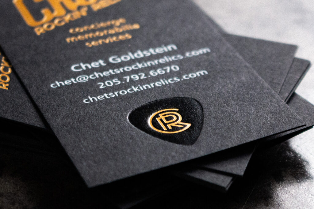 A black business card with white, gold and black foil stamping.